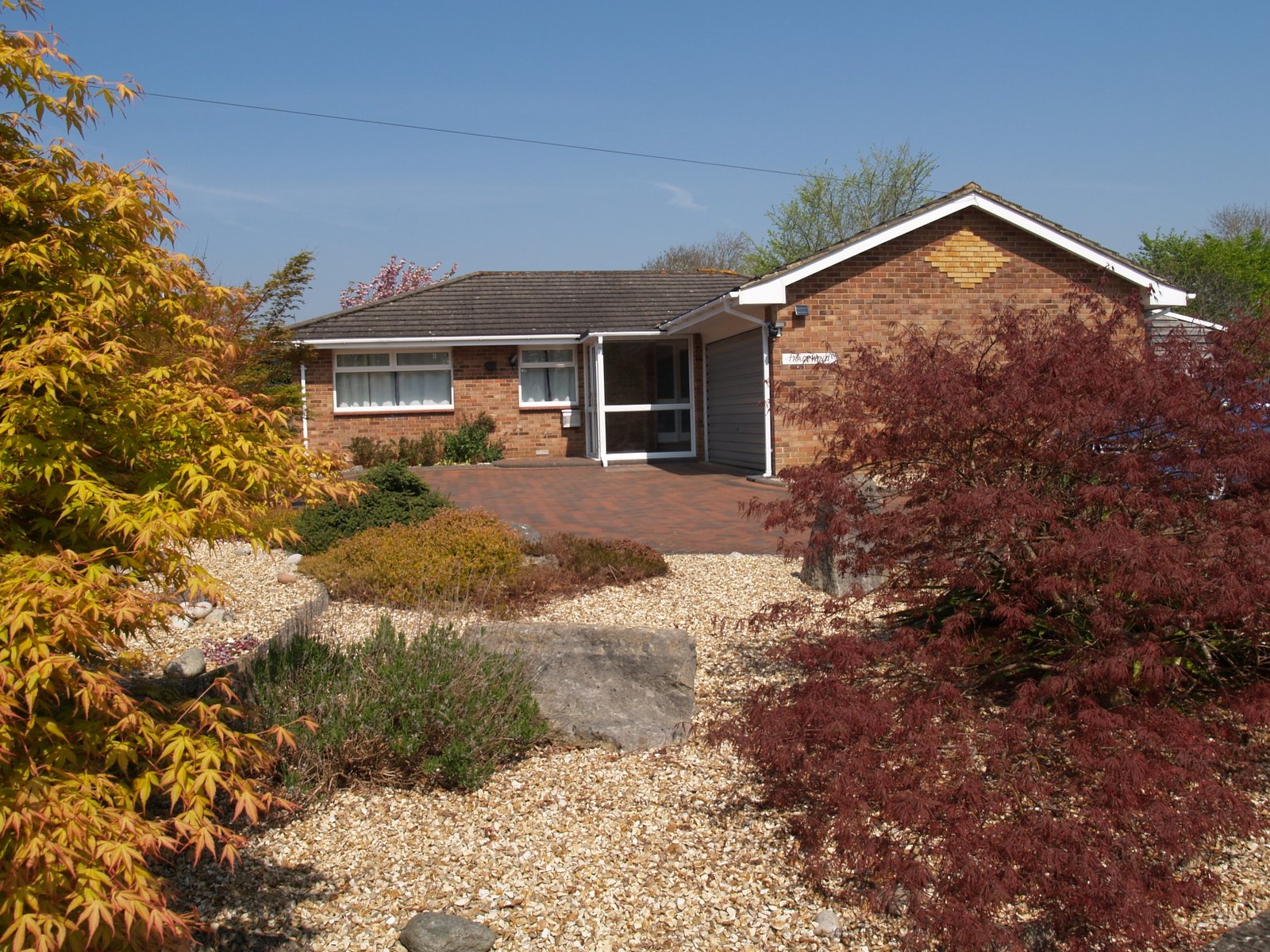 A picture of a bungalow and driveway with a blue sky and gravel garden area on the Isle of Wight